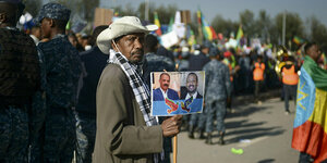 Ein Mann dreht sich zum Fotografen und hält ein Plakat mit Eritreas Präsidenten links, und Äthiopiens Präsidenten rechts in der Handm er trägt einen Hut