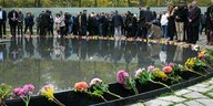 Bunte Blumen sind am Denkmal für die ermordeten Sinti und Roma abgelegt, Menschen spiegeln sich im Wasser des Denkmals