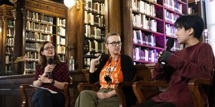 Summer Boismier sitzt mit zwei weiteren Personen in der Bibliothek auf einem Podium