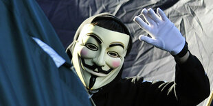 Ein Mensch mit Guy-Fawkes-Maske winkt