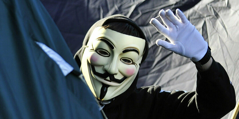 Ein Mensch mit Guy-Fawkes-Maske winkt