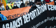 Demonstrant:innen halten ein schwarzes Transparent mit der Aufschrift "against deportation center" hoch