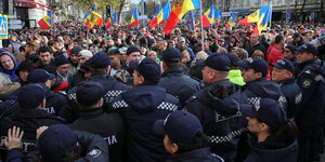 Rücken von Polizisten, die eine Reihe bilden vor Demonstranten mit rot-gelb-blauen Fahnen