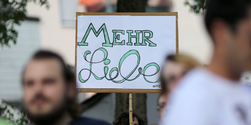 Demonstranten halten ein Schild hoch, auf dem „Mehr Liebe“ steht.