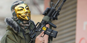 Ein Soldat trägt eine goldene Maske und hält ein Sturmgewehr in der rechten Hand