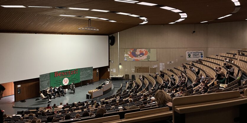 Der besetzte Hörsaal mit Plakaten und einem Podium