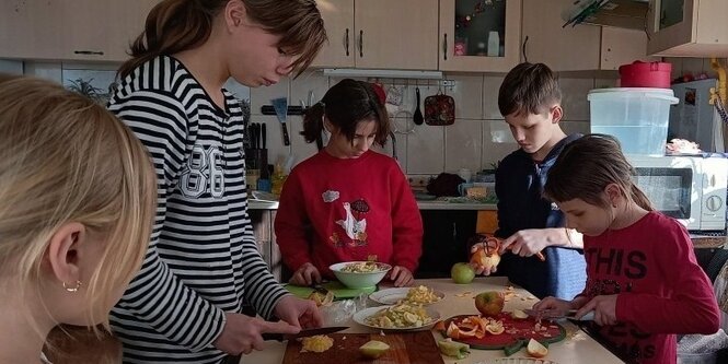 Kinder stehen an einem Esstisch und bereiten eine Mahlzeit zu