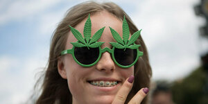 Eine Frau mit grüner Hanfbrille lächelt und trägt eine Zahnspange