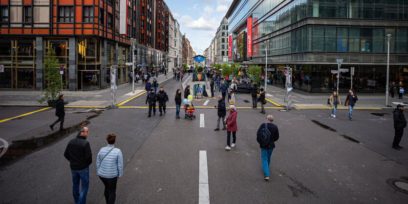 Die autofreie Friedrichstraße. Ein paar Leute gehen auf der noch erkennbaren ehemaligen Fahrbahn. Die Fußwege sind eher Leer. Rechts und links von der Straße große Häuser