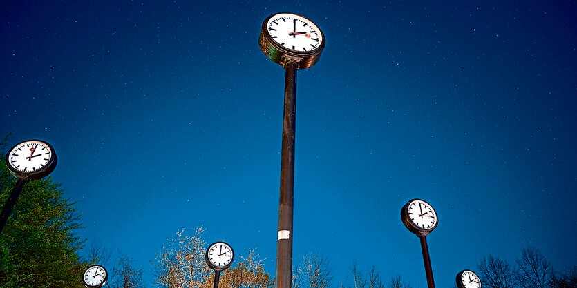 Blauer Himmel, sechs hohe Bahnhofsuhren ragen in ihn