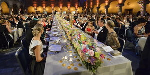 Mit Blumen geschmückte lange Tafen in einem historischen Raum, festlich angezogene Gäste an Tischen