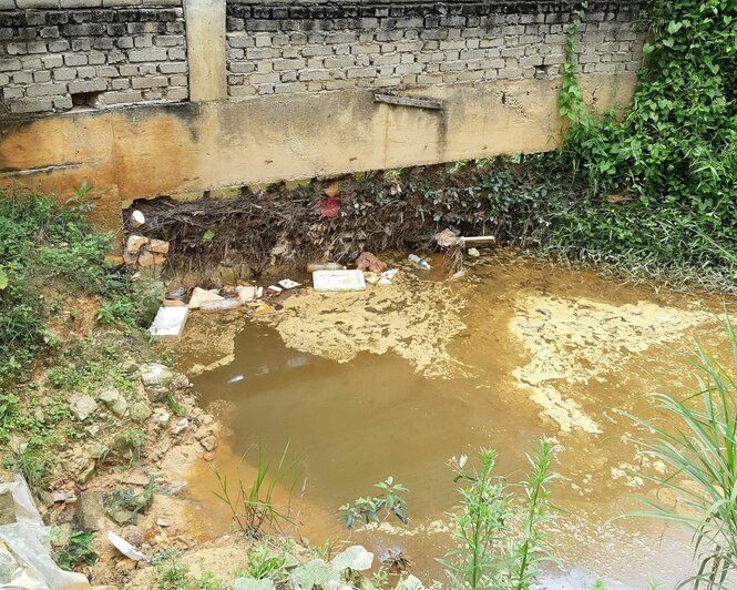 An der Mauer der Sortier- und Zerkleinerungsanlage Polyplast in Malaysia steht ein trübes braun-brackiges Gewässer. Mehrere Plastikflaschen und andere Plastikteile sind zu sehen