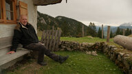 Werner Herzog sitzt auf einer Bank vor einem Haus auf dem Land