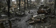Eine Frau geht eine mit Trümmern und zerstörtem Kriegsgerät übersäte Straße entlang.