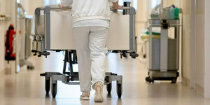 ein Pflegerin von hinten fotografiert schiebt ein Krankenbett über einen Krankenhausflur