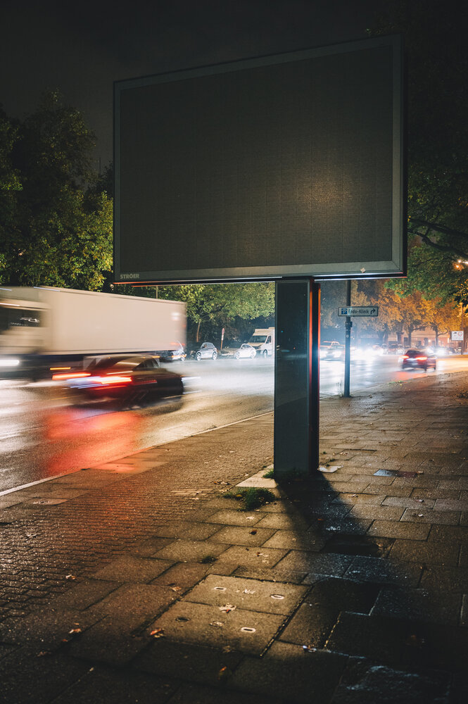 Lichter des Straßenverkehrs in der Nacht hinter ausgeschalteten Reklametafel