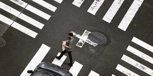 Ein Passant geht über eine Kreuzung bei der auf jeder Straße ein Zebrastreifen ist.