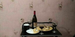 Auf einem kleinen Tisch stehen Weingläser, eine Flasche Rotwein und zwei Teller mit Käse