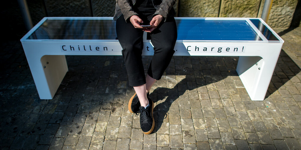 Eine Person sitzt mit ihrem Handy auf einer Bank