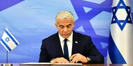 Israelischer Ministerpräsident Lapid unterschreibt ein Papier, im Hintergrund sind Flaggen Israels zu sehen