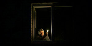 Eine Frau hält eine Kerze und blickt aus dem Fenster bei tiefster Nacht