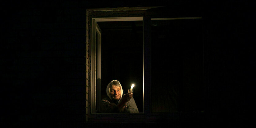 Eine Frau hält eine Kerze und blickt aus dem Fenster bei tiefster Nacht