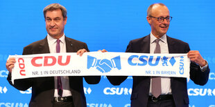 Markus Söder, CSU-Vorsitzender und bayerischer Ministerpräsident (l) und Friedrich Merz,Vorsitzender der CDU, stehen auf der Bühne und halten dabei einen CDU/CSU Fanschal