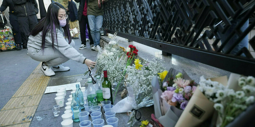 Eine Frau legt Blumen an einer Mauer nieder, wo schon weitere Blumen und Kerzen stehen