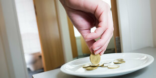 Eine Hand legt ein 50-Cent-Stück auf eine Untertasse mit Kleingeld, vermutlich in einer Toilettenanlage