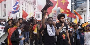 Menschen protestieren, einer hält ein Megafon in die Höhe, manche schwenken rote Fahnen