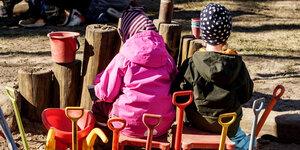 Zwei Kinder, von hinten fotografiert, spielen in der Kita draußen mit vielen Schaufeln
