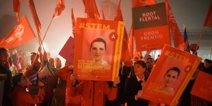 Menschen halten orangene Plakate und Fahnen in die Höhe