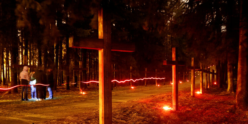 Holzkreuze in einer Reihe, unter jedes ist ein Trauerlicht gestellt