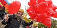 Eine Frau hält einen Strauß mit roten Luftballons in die Höhe