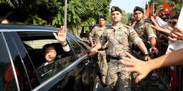 Libanons Präsident Michel Aoun sitzt in einem Auto und winkt. Das Auto wird von Soldaten eskortiert.