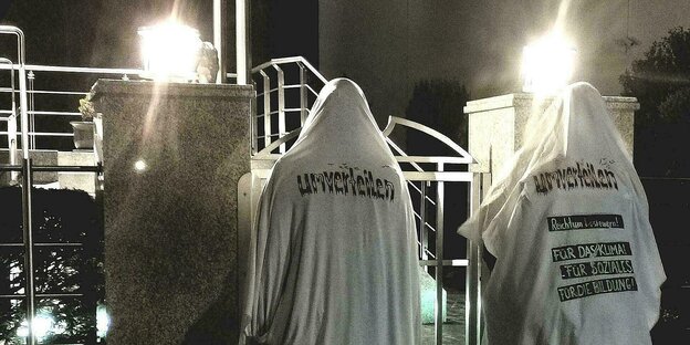 Drei als Gespenster verkleidete Aktivist:innen stehen nachts vor einer Villa. Auf dem Rücken eines Gespensts ist "Umverteilen - Reichtum besteuern für das Klima, für Soziales, für die Bildung" zu lesen.