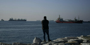 Eine Person schaut auf das Meer, auf dem Cargoschiffe schwimmen