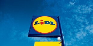 Ein Schild mit "Lidl"-Logo vor einem blauen Himmel.