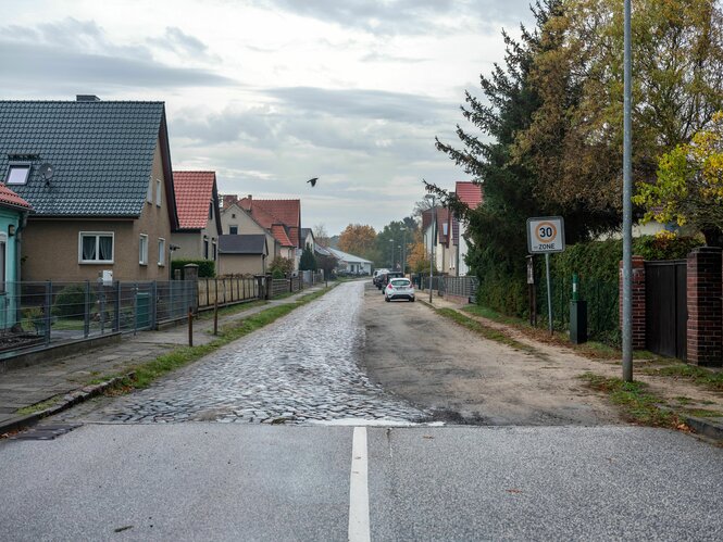 im Dorf geht eine asphaltierte Straße in Kopfsteinpflaster über