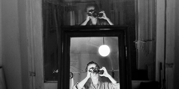 Eine Frau fotografiert sich im Spiegel und spiegelt sich darüber auch in der Fensterscheibe