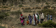 Frauen, Kinder und Männer laufen durch eine Savannenlandschaft