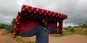 Ein Mann trägt ein buntes Sofa durch eine überflutete Landschaft