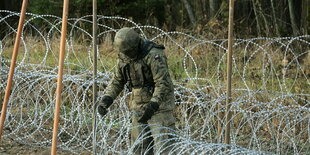 Ein Soldat hantiert an einem Stacheldrahtzaun