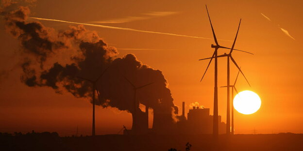 Windräder vor Sonnenuntergang hinter einem Kraftwerk mit Dampfwolke.