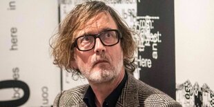 Jarvis Cocker trägt eine Brille mit schwarzem Rand und hat dunkelblonde lange Haare