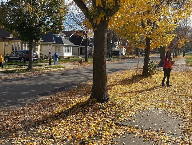 Wohnviertel mit Bäumen und Herbstlaub auf den Straßen, junge Leute mit Broschüren unterwegs