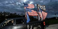 Ein Truck mit US-Flaggen und eine Flagge mit der Info: "Fuck Biden" fährt durch die Dämmerung