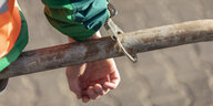Eine Hand ist mit einer Handschelle an eine Eisenstange gekettet