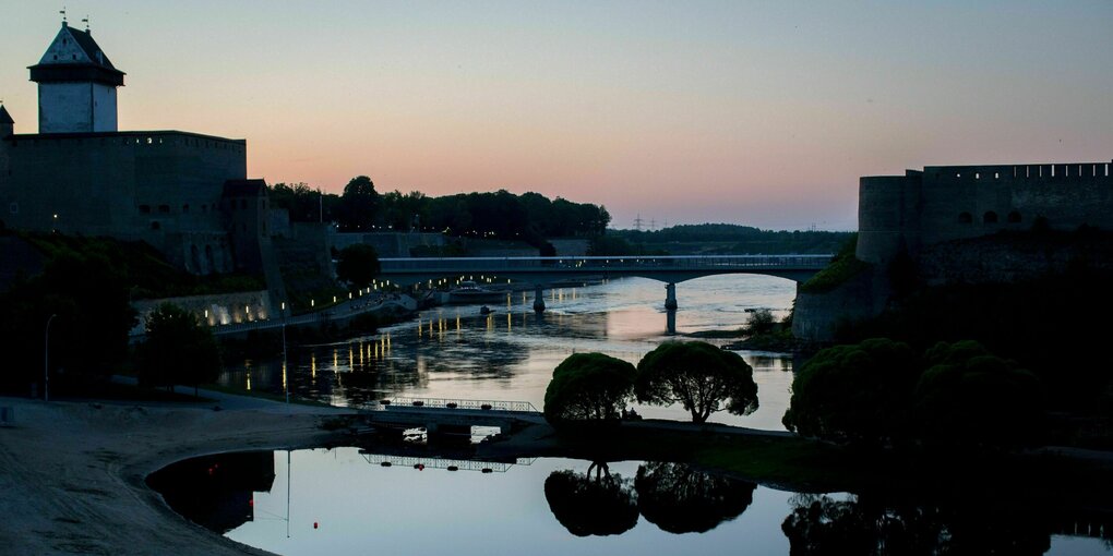 Sonnenuntergang hinter der estnischen Stadt Narva und der russischen Burg Iwangorod auf der gegenüberliegenden Seite unter, getrennt durch den Fluss Narva