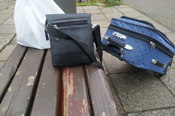 Eine keline Tasche und ein Rollkoffer stehen an einer Bank